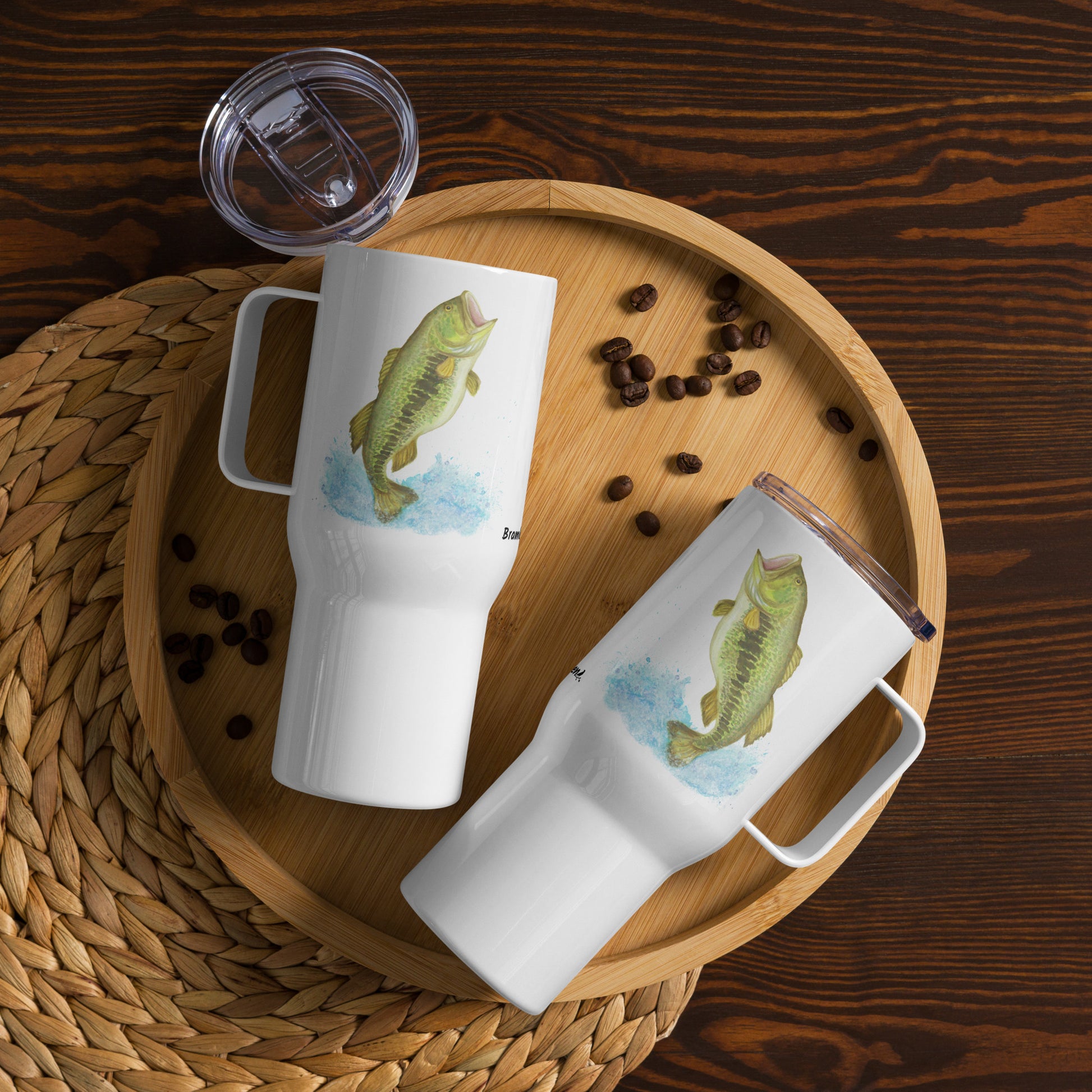 Stainless steel travel mug with handle. Holds 25 ounces of hot or cold drinks. Has print of watercolor bass fish on both sides. Fits most car cup holders. Comes with spill-proof BPA-free plastic lid. Two mugs shown on wooden tray by coffee beans.