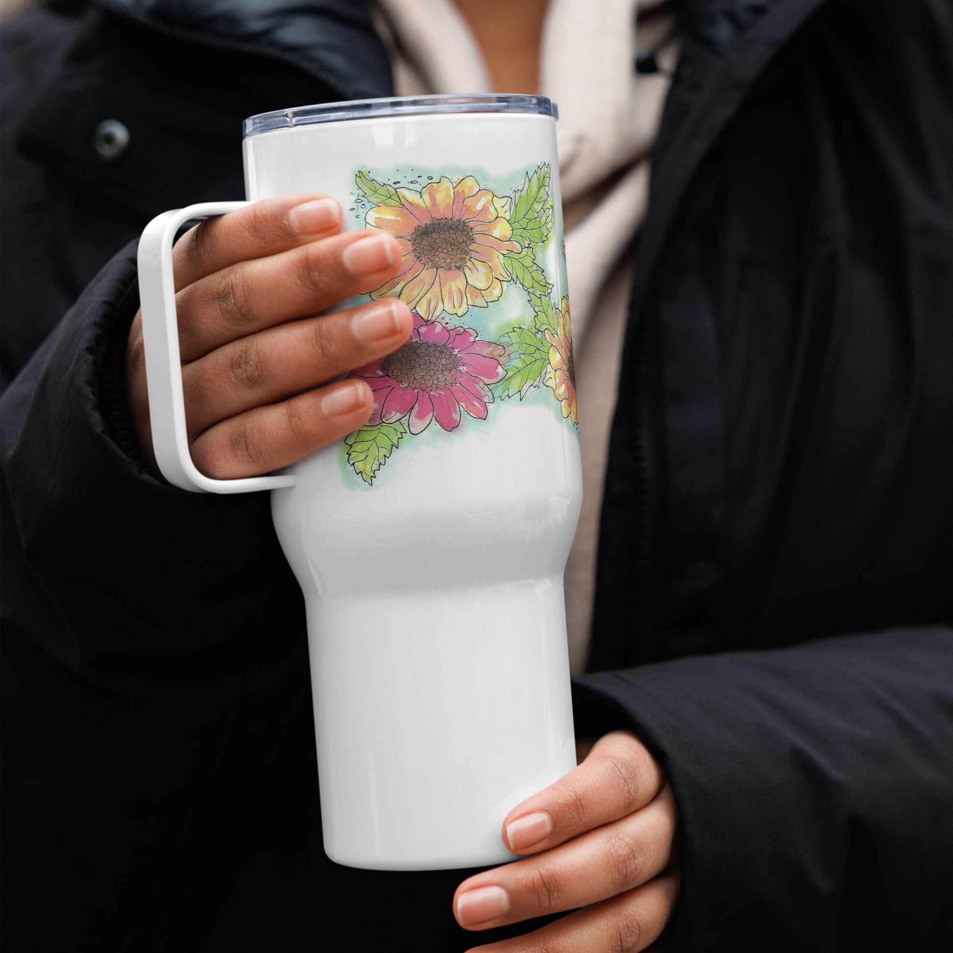 Gerber daisies stainless steel travel mug with handle. Holds 25 ounces and has a BPA-free plastic lid. Shown in model's hands.
