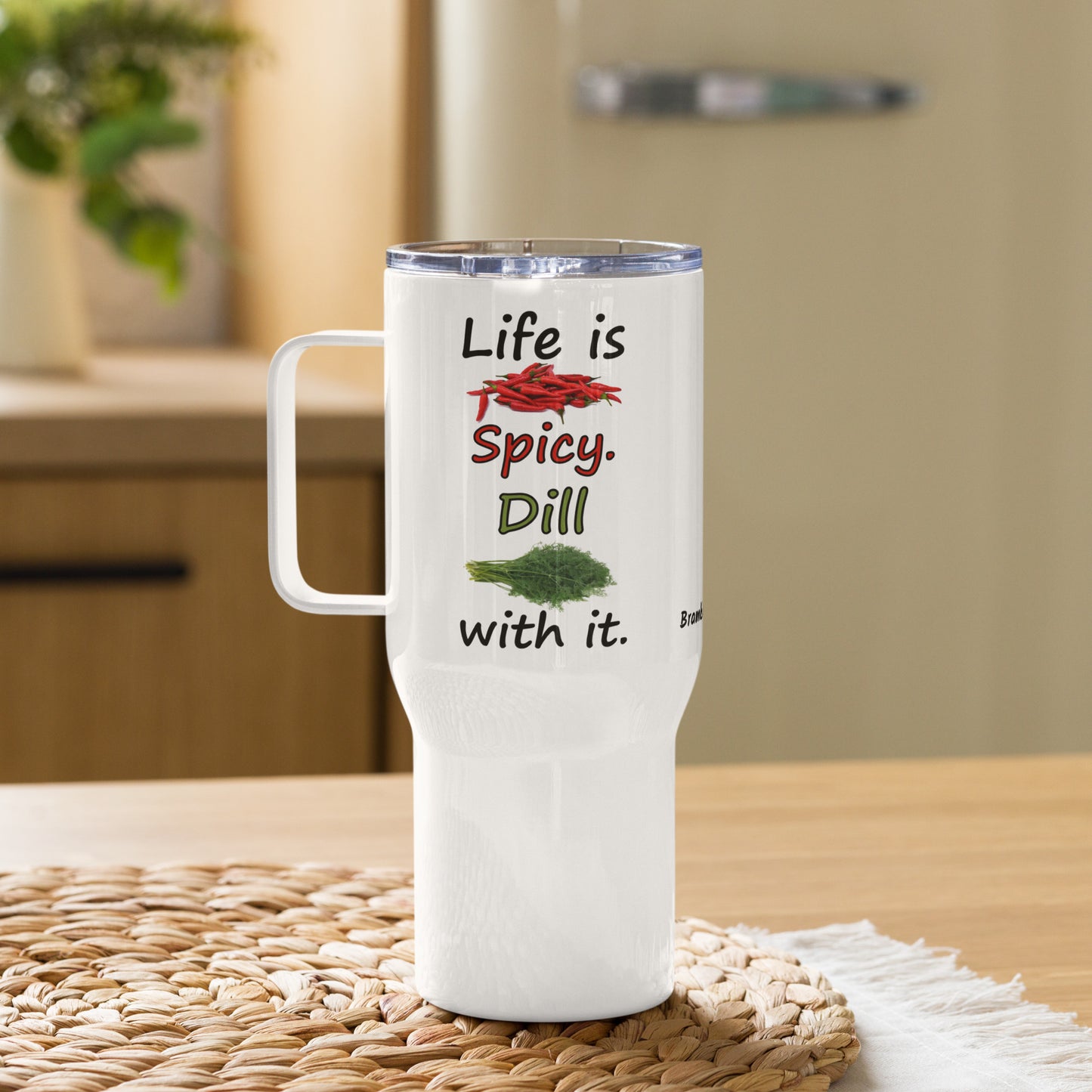 Stainless steel travel mug with handle. Holds 25 ounces of hot or cold liquids. Fits most car cup holders. Features double-sided phrase: Life is spicy. Dill with it, and accompanying chili pepper and dill weed images. Comes with spill proof plastic lid. Shown on tabletop.