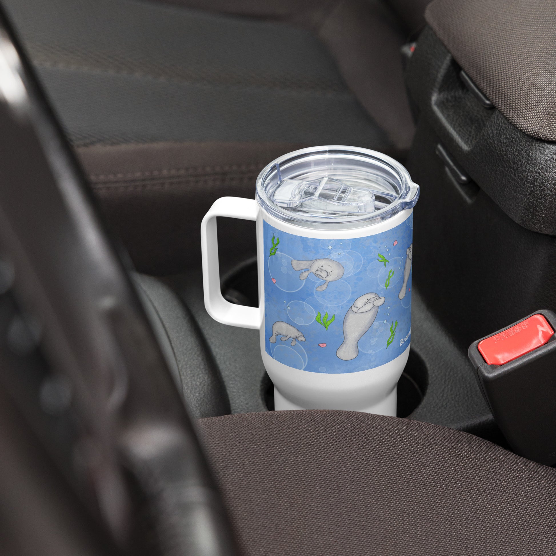 Stainless steel travel mug with handle. Holds 25 ounces of hot or cold drinks. Has wraparound illustrated manatees design. Fits most car cup holders. Comes with spill-proof BPA-free plastic lid. Shown in car cup holder with handle facing left.