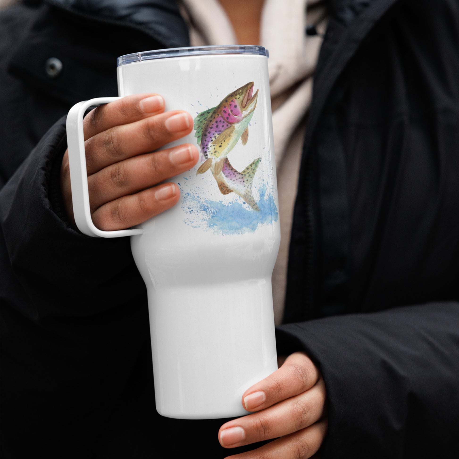 Stainless steel travel mug with handle. Holds 25 ounces of hot or cold drinks. Has print of watercolor rainbow trout fish on both sides. Fits most car cup holders. Comes with spill-proof BPA-free plastic lid. Shown in model's hands.