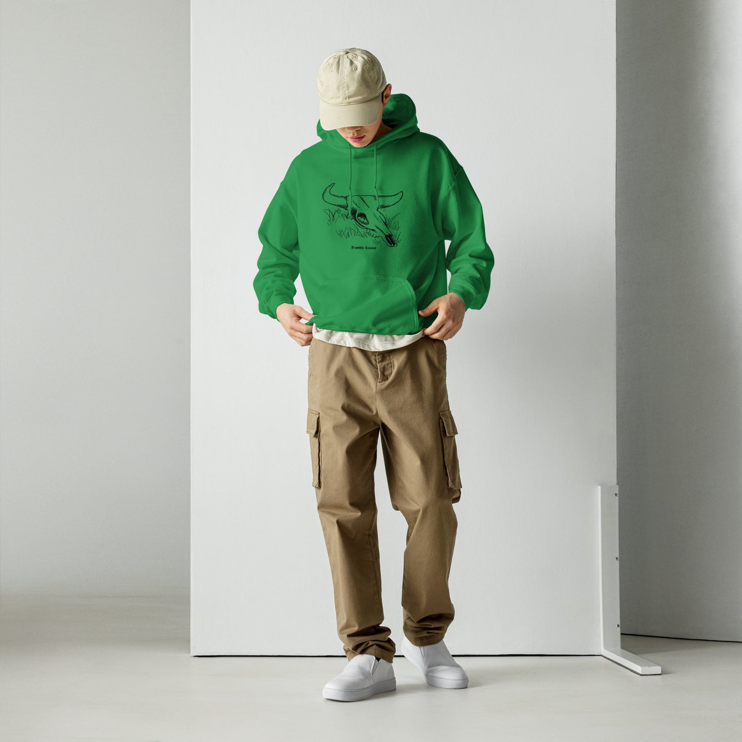 Irish green colored unisex hoodie. Front has image of a cow skull cradling a bird nest. Features double-lined hood and front pouch pocket. Shown on male model with khaki pants and baseball cap.