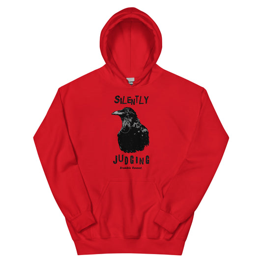 Unisex red colored hoodie with vertical design of silently judging text above and below black crow wearing a monocle.  Design on the front of hoodie. Features double-lined hood and front pouch pocket.