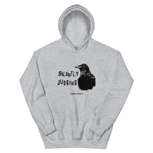 Unisex sport grey colored hoodie with horizontal design of silently judging text by black crow wearing a monocle.  Design on the front of hoodie. Features double-lined hood and front pouch pocket.