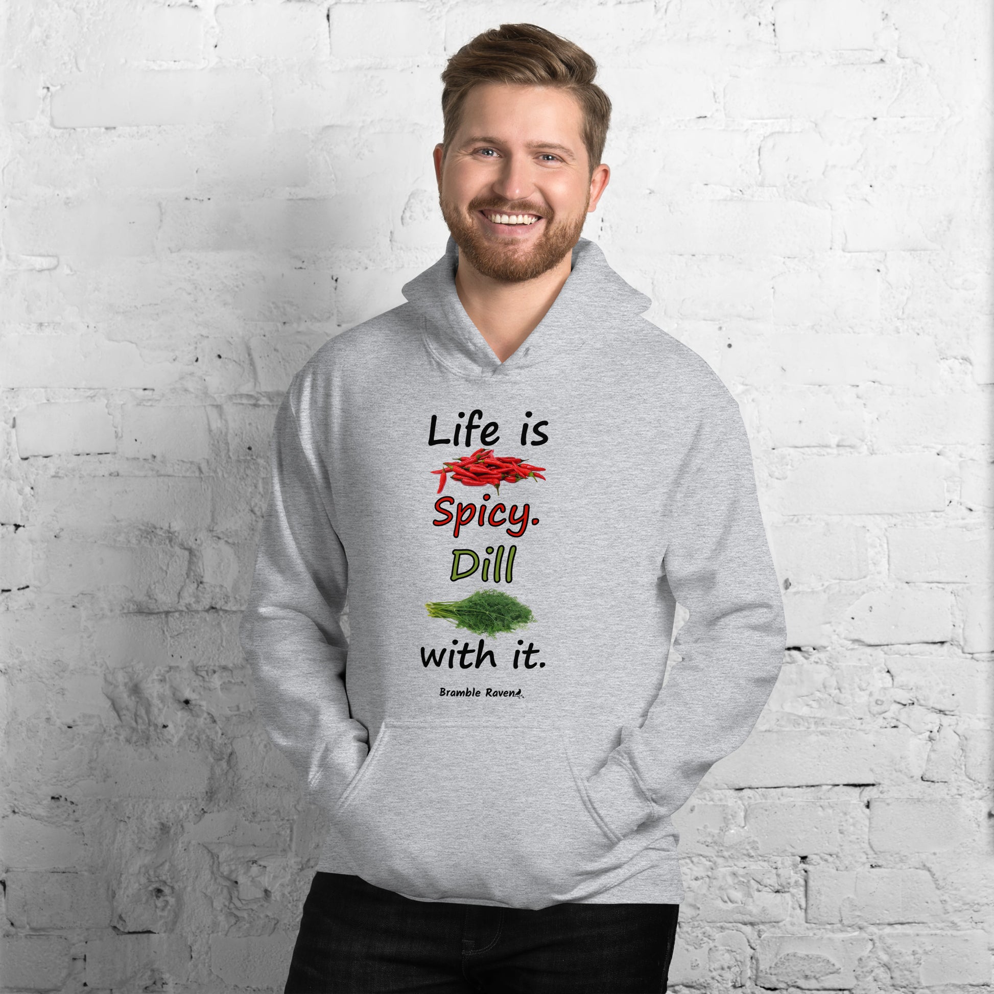 Sport grey colored unisex heavy blend hoodie.  Double lined hood, matching drawcord, front pouch pocket. Rib knit cuffs and waistband. Features text and image: Life is spicy. Dill with it.  Shown on male model against brick wall.