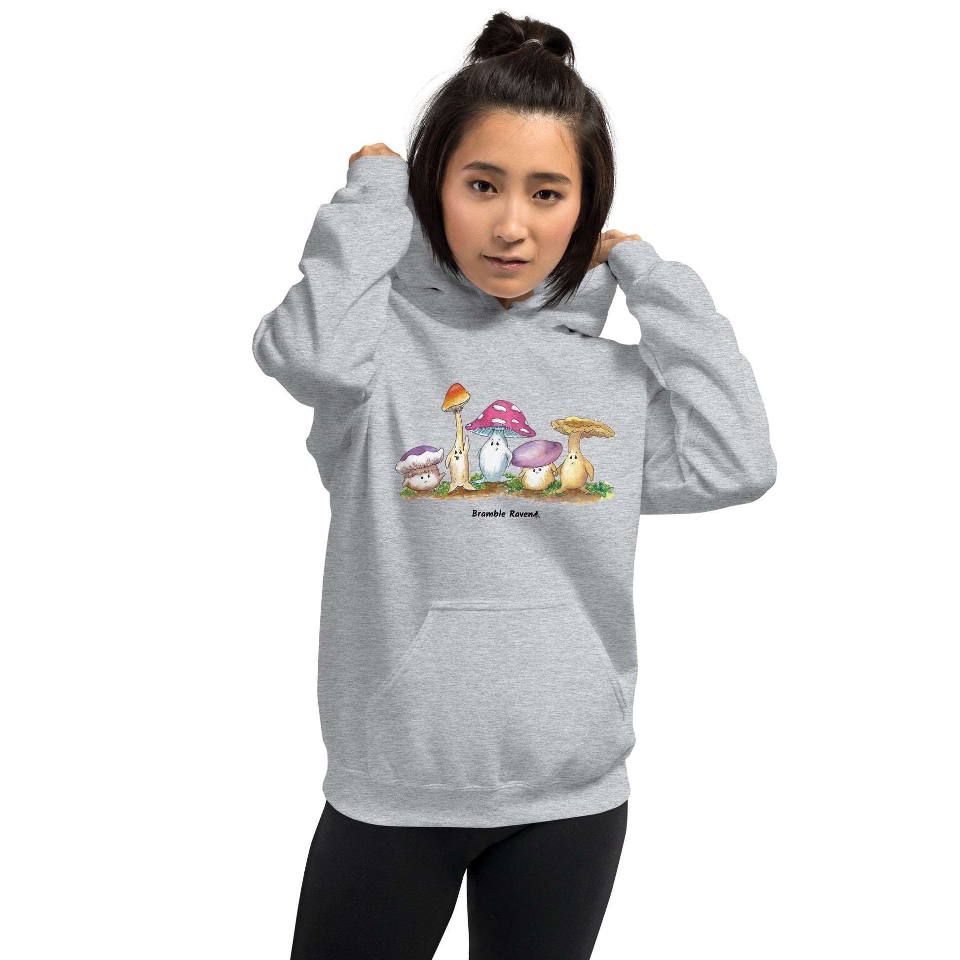 Sport grey colored unisex cotton/polyester blend hoodie. Features front design of Mushy and his whimsical mushroom friends. Hoodie has double lined hood, front pouch pocket, rib knit cuffs and stretchy waistband. Shown on female model.