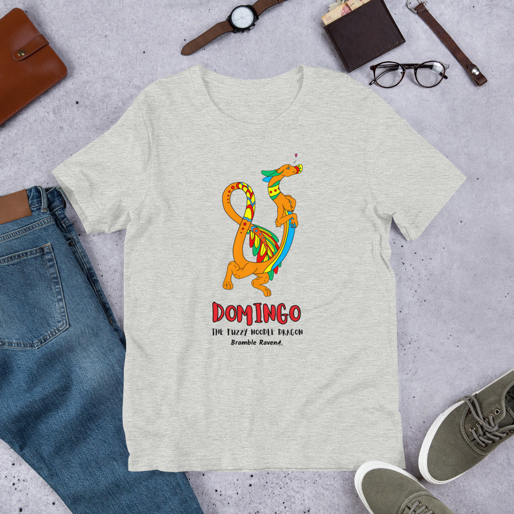 Domingo the Fuzzy Noodle Dragon on an athletic heather grey unisex t-shirt. Shown surrounded by pants, shoes, glasses, a watch, and wallet.