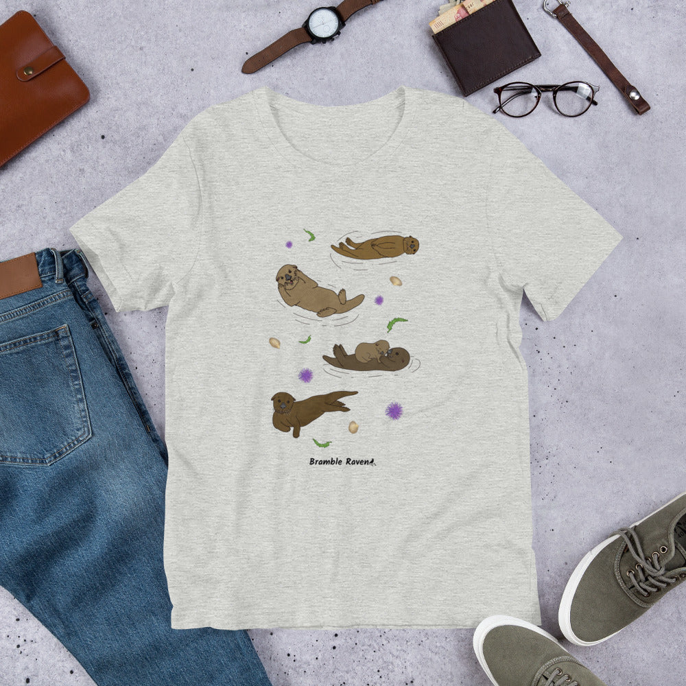 Unisex athletic heather grey colored t-shirt. Features four sea otters with seaweed, shells, and sea urchins. Shown surrounded by pants, shoes, and a wallet.