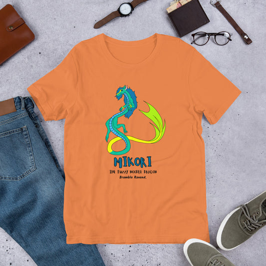 Mikori the Fuzzy Noodle Dragon on a burnt orange unisex t-shirt. Shown surrounded by pants, shoes, glasses, a watch, and wallet.