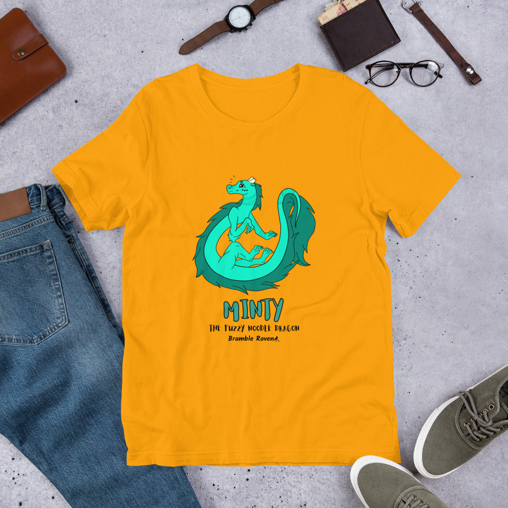 Minty the Fuzzy Noodle Dragon on a gold unisex t-shirt. Shown surrounded by pants, shoes, glasses, a watch, and wallet.