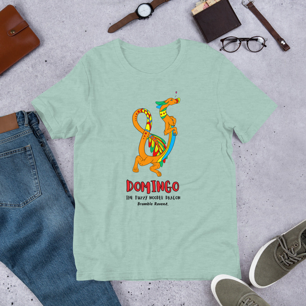Domingo the Fuzzy Noodle Dragon on a heather prism dusty blue unisex t-shirt. Shown surrounded by pants, shoes, glasses, a watch, and wallet.
