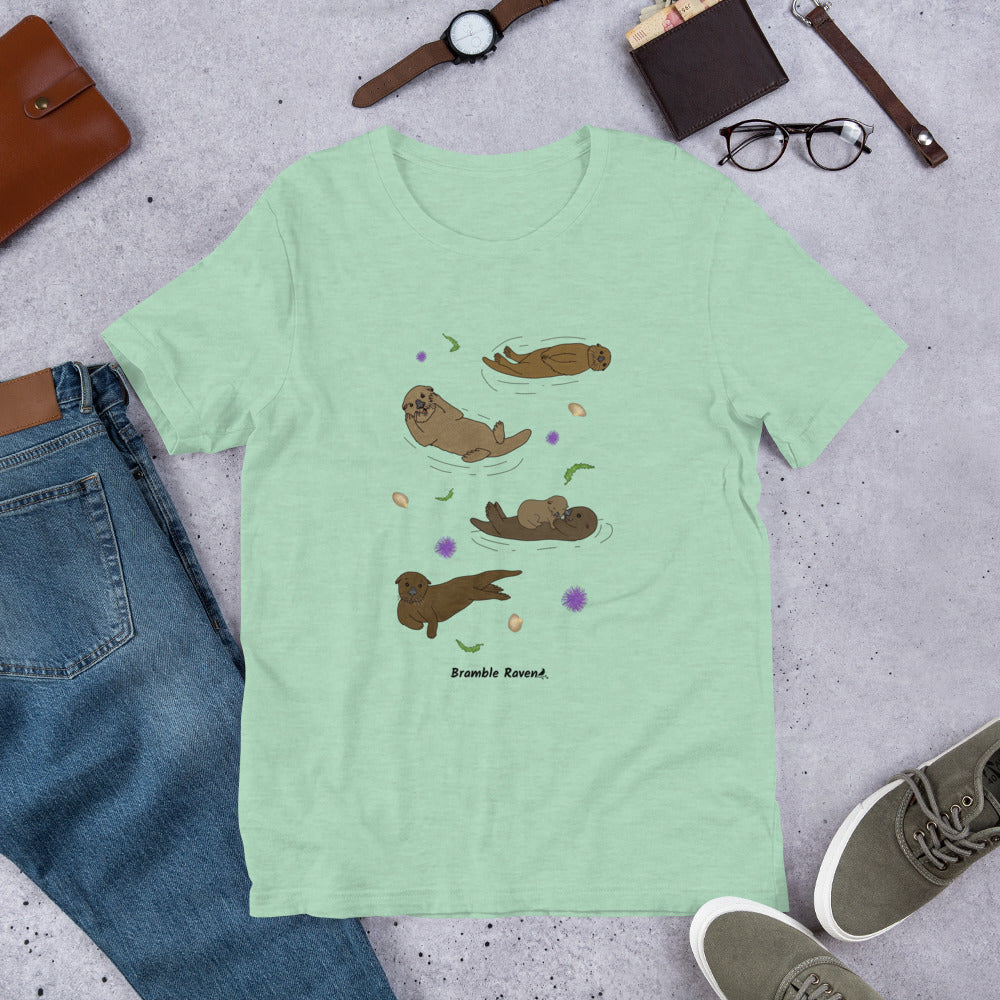 Unisex heather prism mint green colored t-shirt. Features four sea otters with seaweed, shells, and sea urchins. Shown surrounded by pants, shoes, and a wallet.