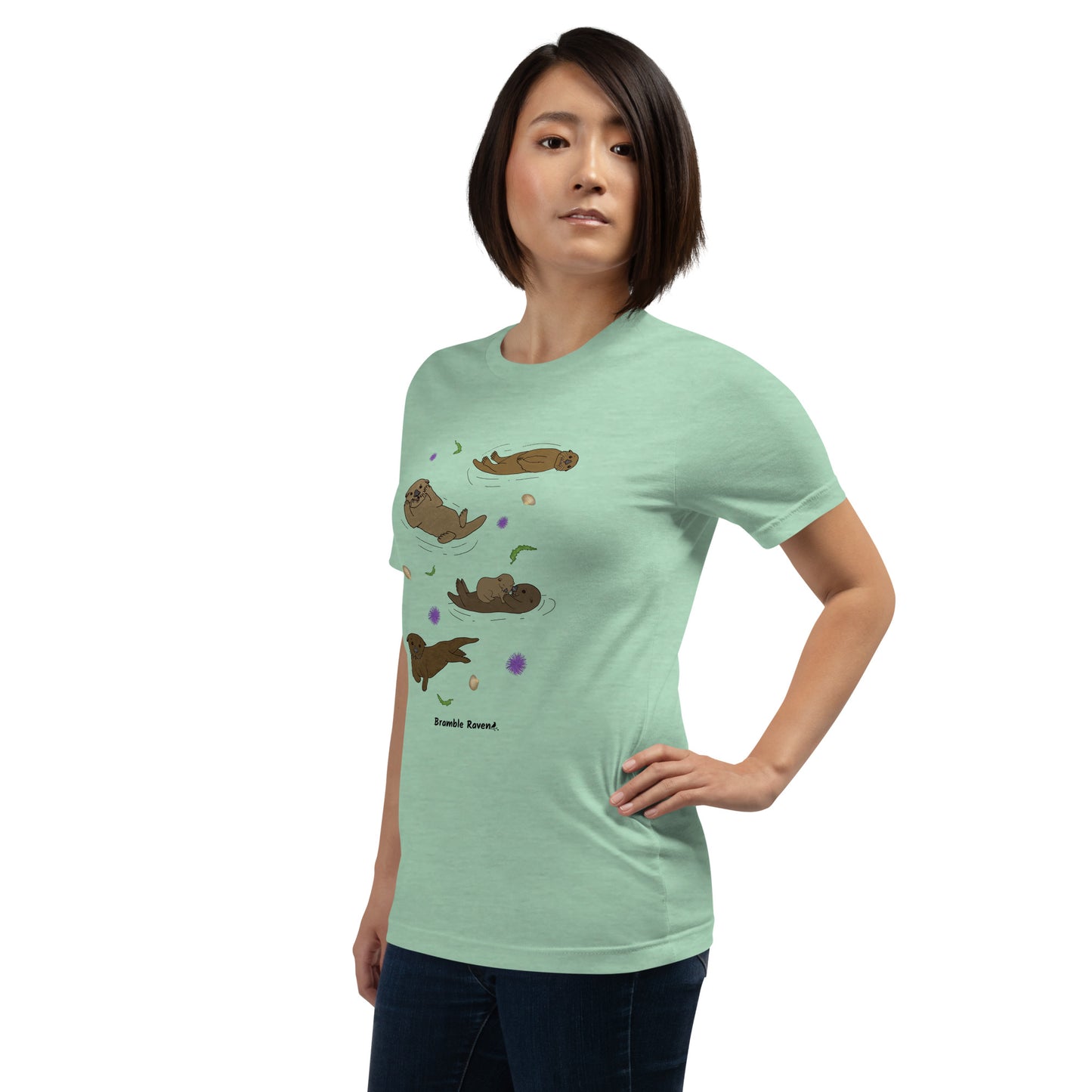Unisex heather prism mint green colored t-shirt. Features four sea otters with seaweed, shells, and sea urchins. Shown on female model facing left.