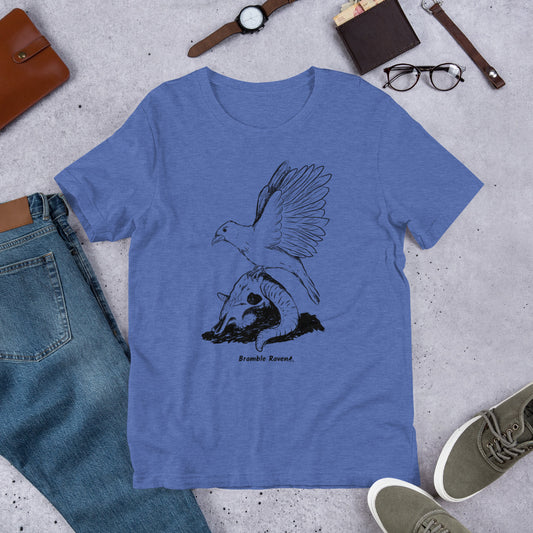 Royal blue colored unisex t-shirt. Features Reflections illustration of a crow with wings outstretched sitting on a sheep skull. Shown on floor by pants and shoes.