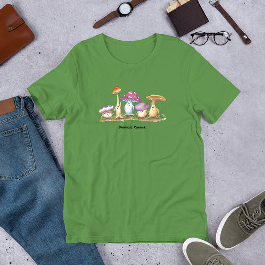 Leaf green colored unisex t-shirt. Features print of Mushy and Friends watercolor painting on front. Shown on floor by jeans, shoes, and glasses.