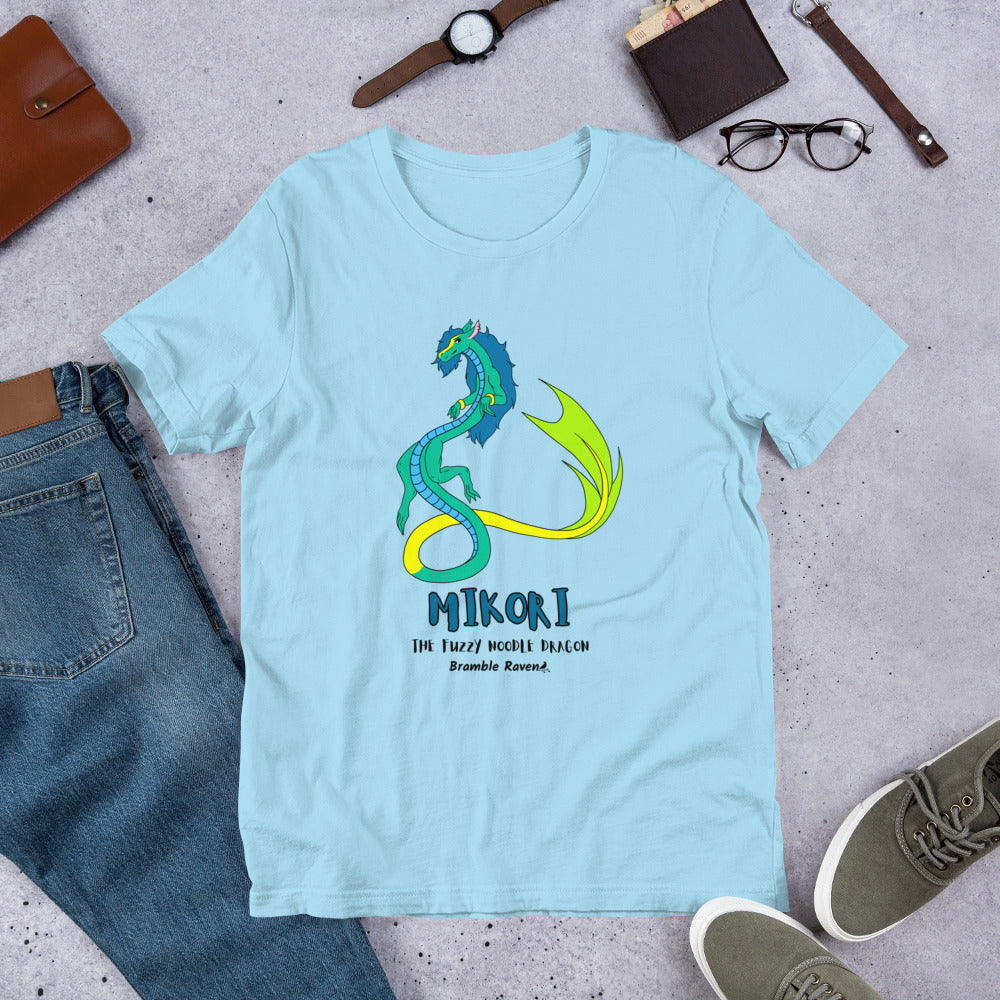 Mikori the Fuzzy Noodle Dragon on an ocean blue unisex t-shirt. Shown surrounded by pants, shoes, glasses, a watch, and wallet.