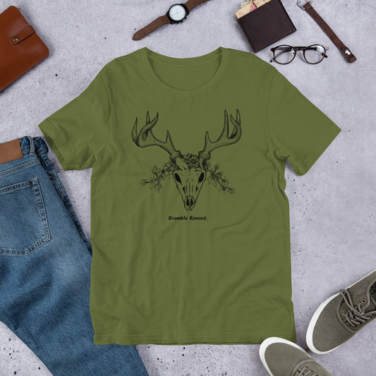 Olive colored unisex t-shirt made from preshrunk cotton. Features hand-designed deer skull wreathed in flowers on front. Available in size XS-5XL. Shown on floor by shoes, pants, wallet, watch, and glasses.