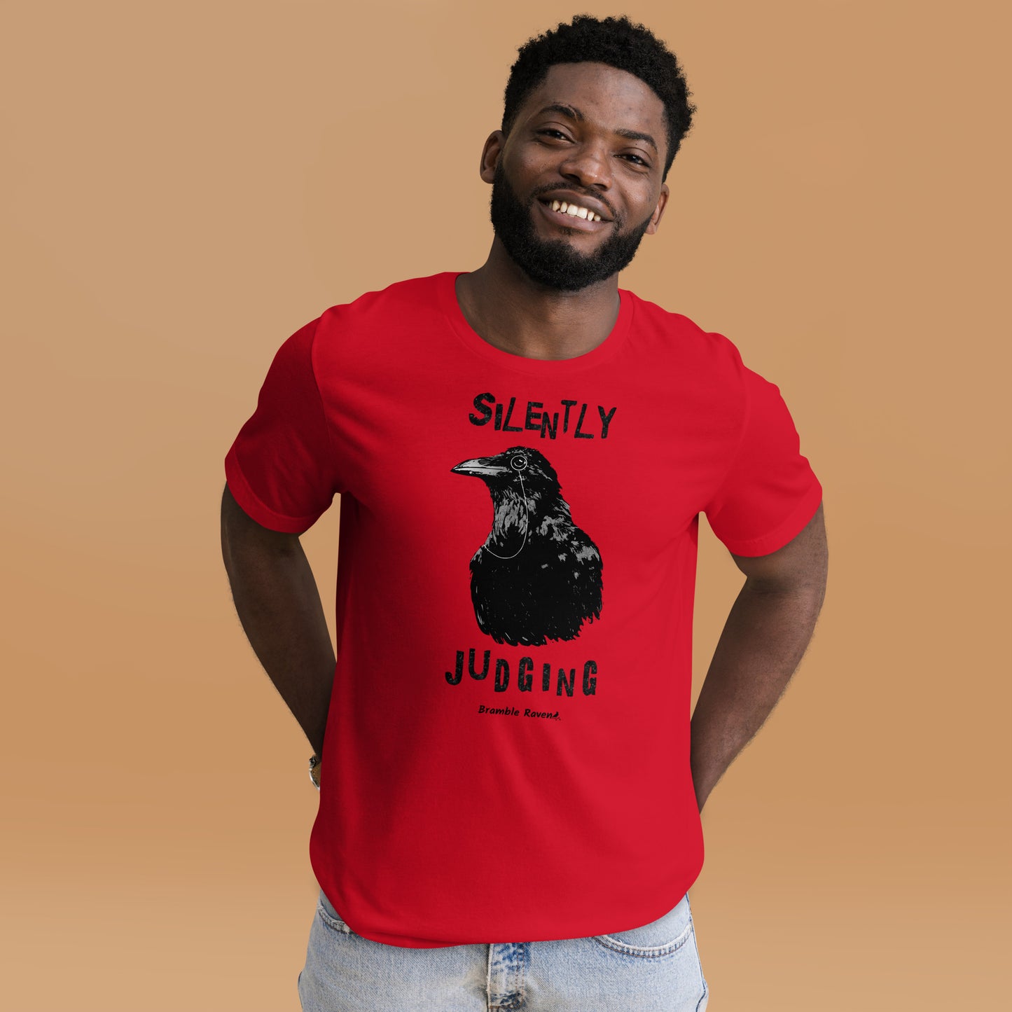 Unisex red colored t-shirt. Features vertical image of silently judging text above and below black crow wearing a monocle.  Shown on male model.