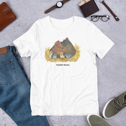White colored unisex t-shirt. Features watercolor mother hen and chicks in a nest printed on the front. Flat lay view by jeans and shoes.