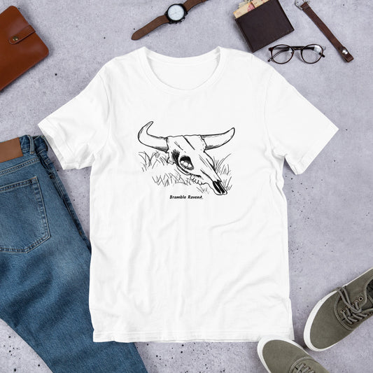  White unisex t-shirt. Features hand designed illustration of a cow skull cradling a bird nest. Shown on floor by pants and shoes.