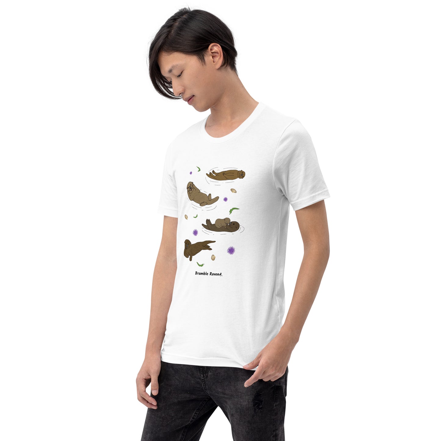 Unisex white colored t-shirt. Features four sea otters with seaweed, shells, and sea urchins. Shown on male model looking left.