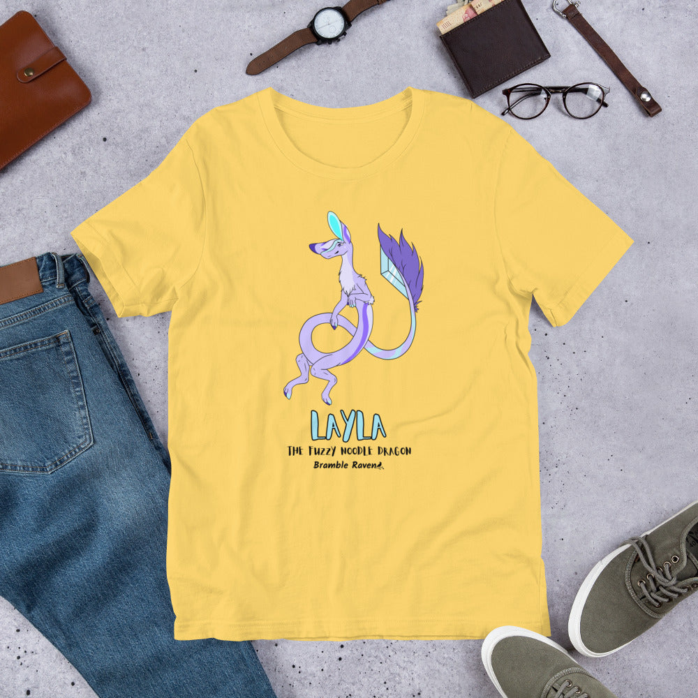 Layla the Fuzzy Noodle Dragon on a yellow unisex t-shirt. Shown surrounded by pants, shoes, glasses, a watch, and wallet.