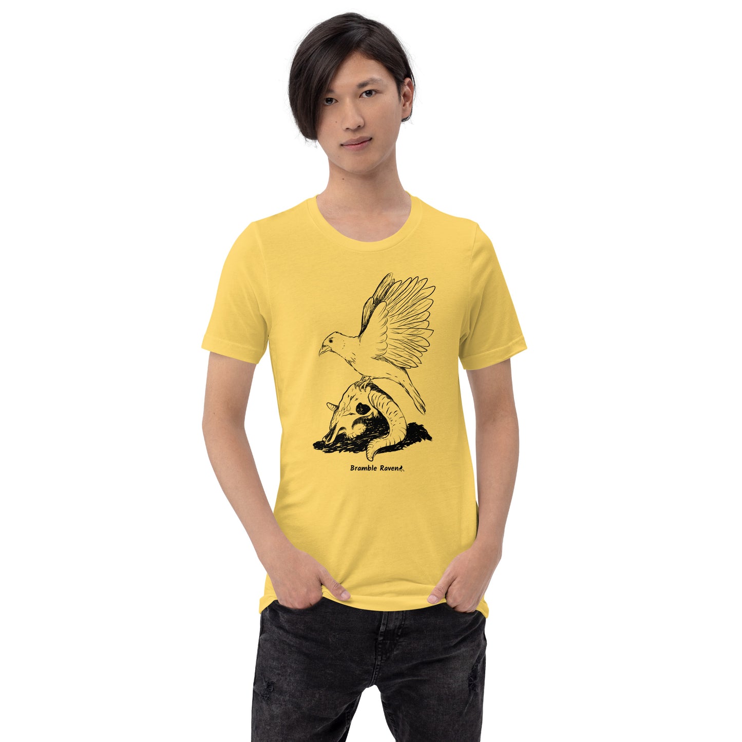 Yellow colored unisex t-shirt. Features Reflections illustration of a crow with wings outstretched sitting on a sheep skull. Shown on male model.