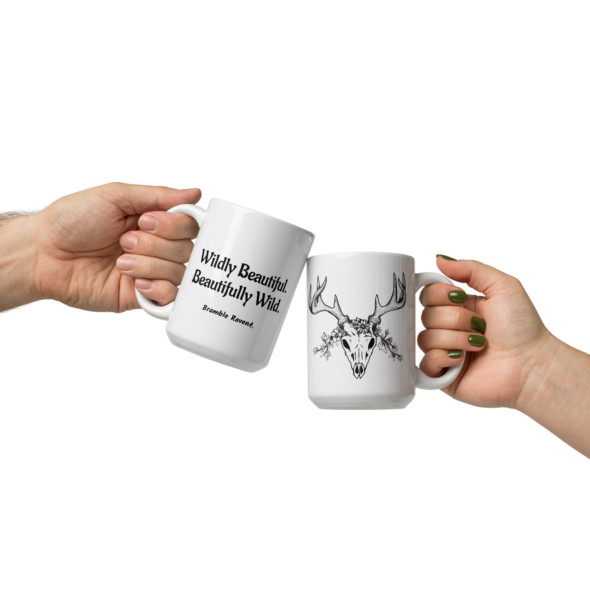 15 ounce white ceramic mug. Features hand-illustrated deer skull wreathed in flowers on one side, and text wildy beautiful, beautifully wild on the other side. Shown in models' hands.