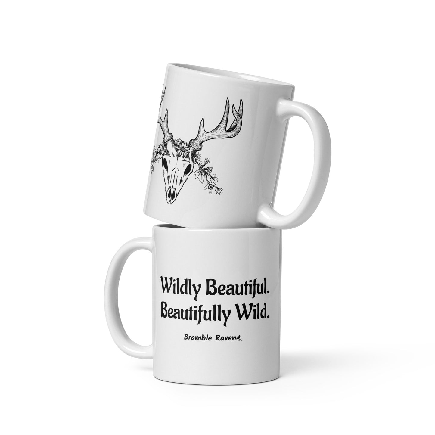 11 ounce white ceramic mug. Features hand-illustrated deer skull wreathed in flowers on one side, and text wildy beautiful, beautifully wild on the other side.