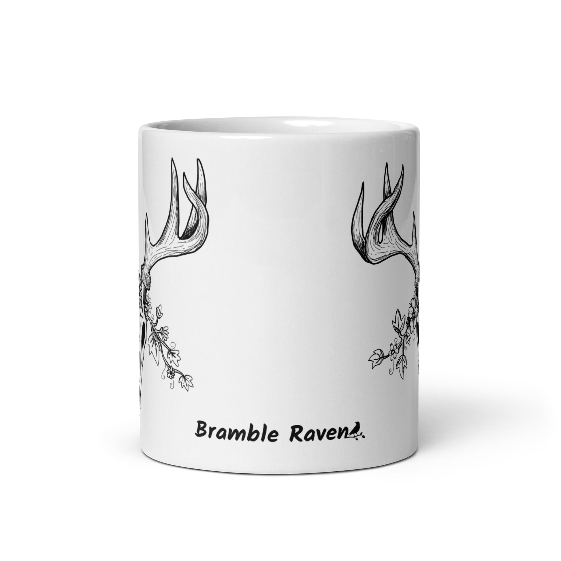 11 oz white ceramic mug. Features a double-sided hand illustrated image of a deer skull wreathed in flowers. Front view shows Bramble Raven logo.