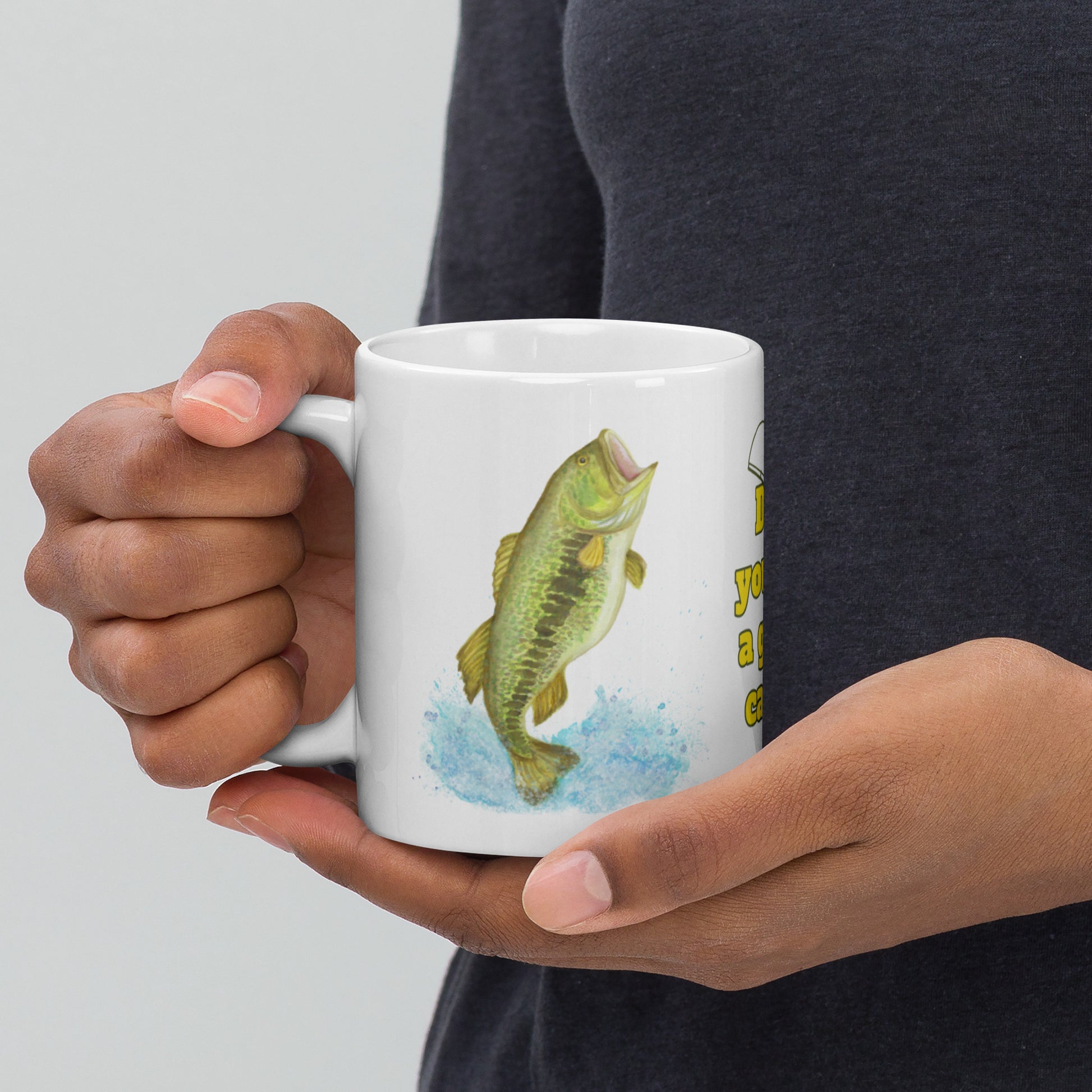 11 ounce ceramic mug. Features watercolor print of a rainbow trout and a largemouth bass with text that says: Dad, you are a great catch! Shown in hand of model.