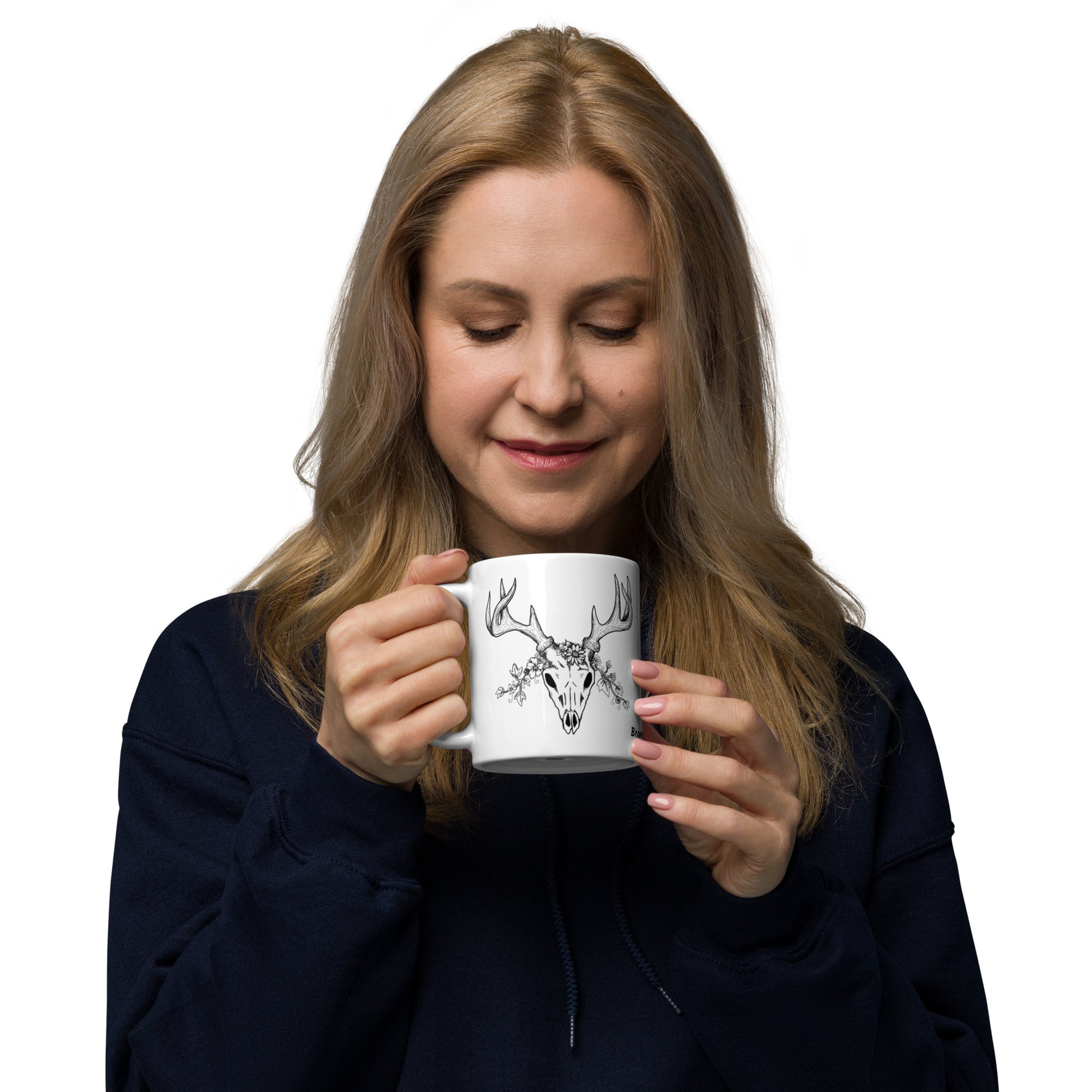 11 oz white ceramic mug. Features a double-sided hand illustrated image of a deer skull wreathed in flowers. Shown in female model's hand.