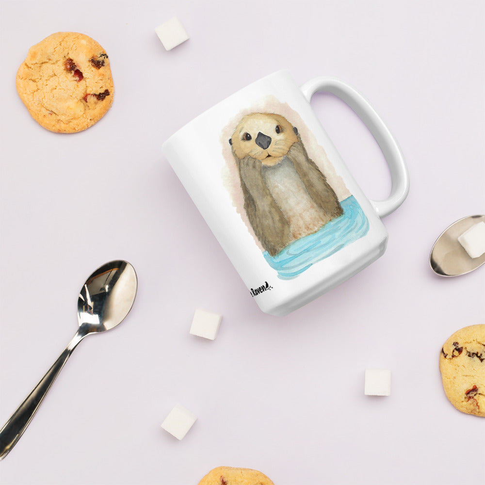 15 ounce white ceramic mug featuring watercolor print of a sea otter on both sides. Dishwasher and microwave safe. Shown on tabletop by cookies, spoon, and sugar cubes.