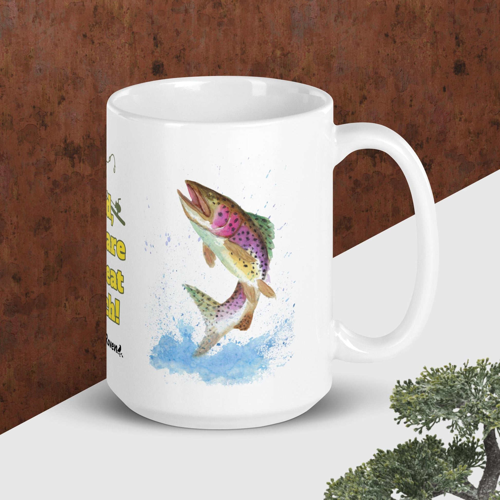 15 ounce ceramic mug. Features watercolor print of a rainbow trout and a largemouth bass with text that says: Dad, you are a great catch! Shown on tabletop with handle facing right.