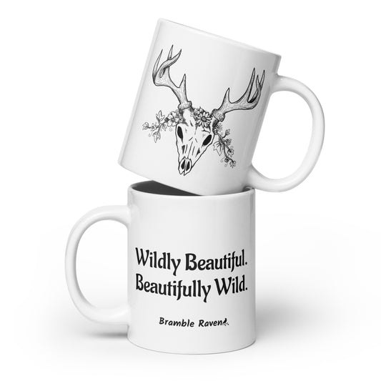 20 ounce white ceramic mug. Features hand-illustrated deer skull wreathed in flowers on one side, and text wildy beautiful, beautifully wild on the other side.