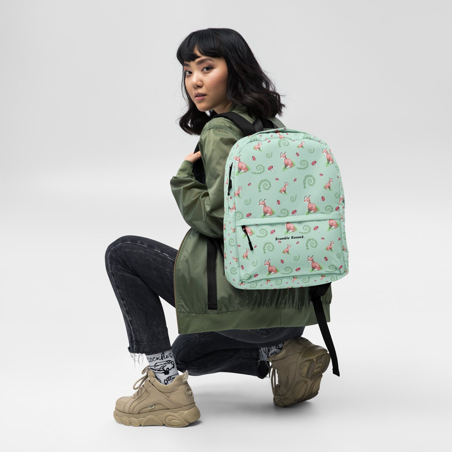 Forest fox backpack. Has watercolor foxes, mushrooms and ferns on a light green water-resistant polyester fabric. Includes an inner pocket that can hold a 15 inch laptop. Has a hidden pocket with zipper on the back, and ergonomic straps. Shown on female model.