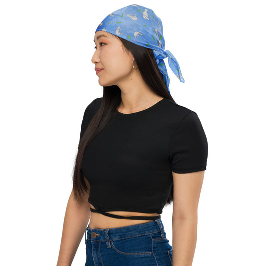 Manatee bandana. Shown as a head bandana on a female model. Features patterned design of hand-illustrated manatees, seaweed, seashells, and bubbles on a blue  background.