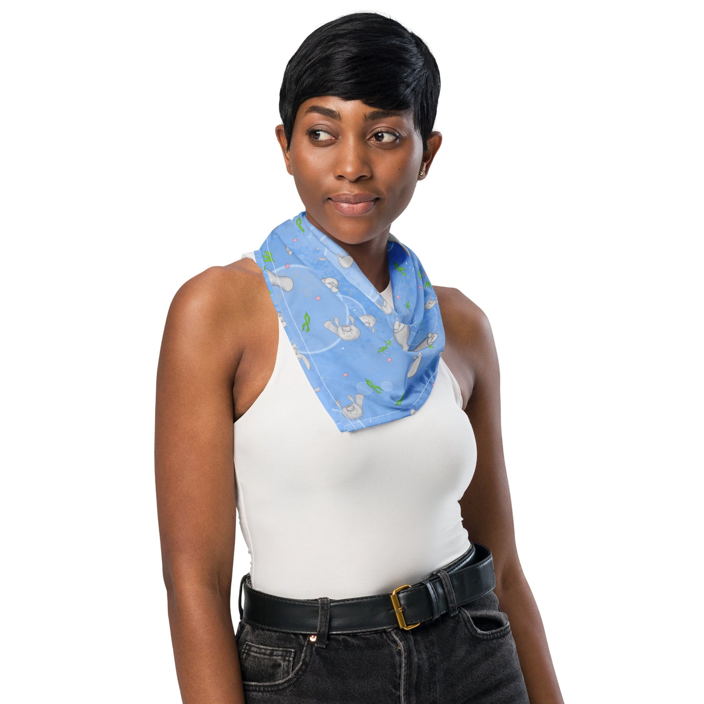 Manatee bandana. Shown as a neck scarf on a female model. Features patterned design of hand-illustrated manatees, seaweed, seashells, and bubbles on a blue  background.