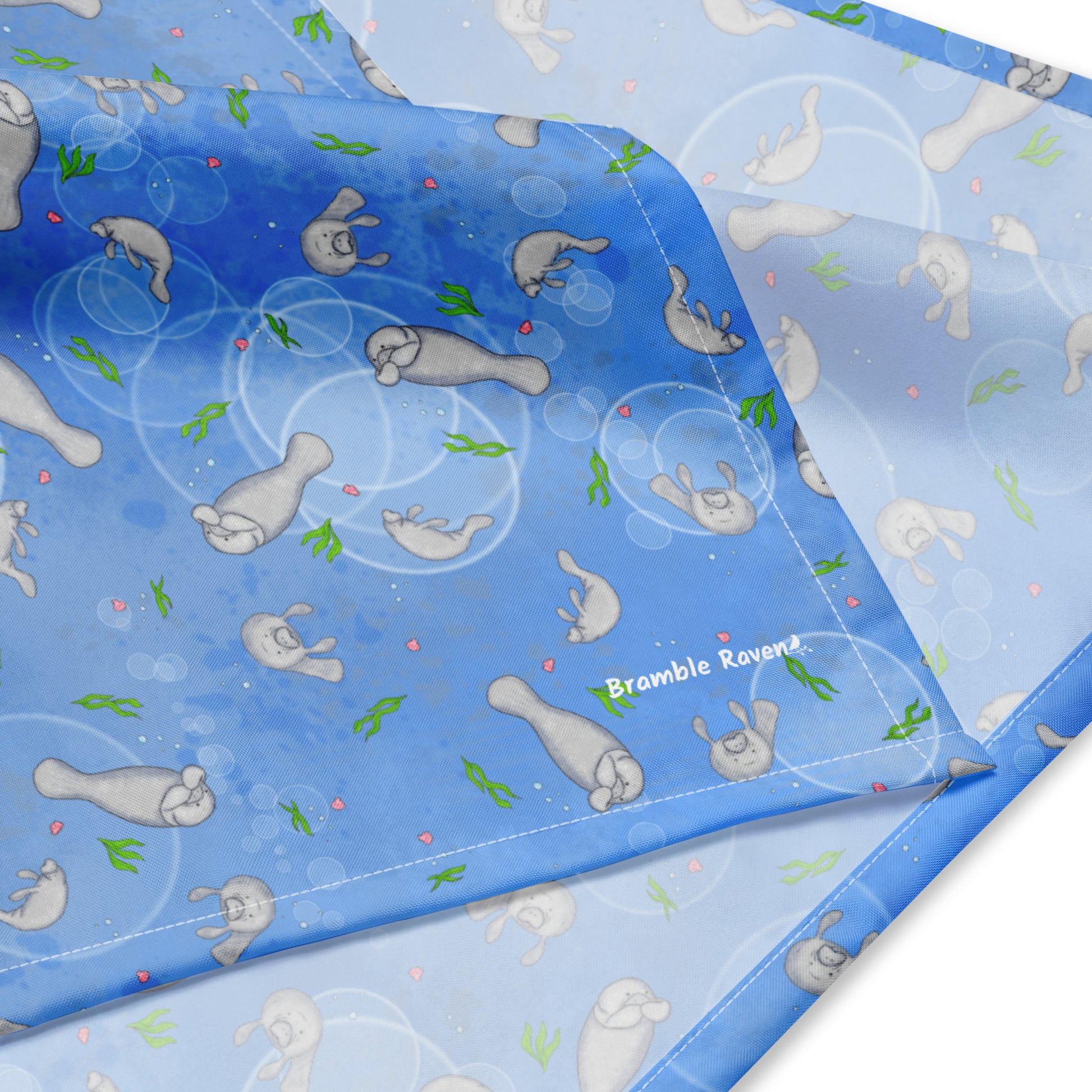 Manatee bandana. Features patterned design of hand-illustrated manatees, seaweed, seashells, and bubbles on a blue  background. Made of microfiber polyester fabric.