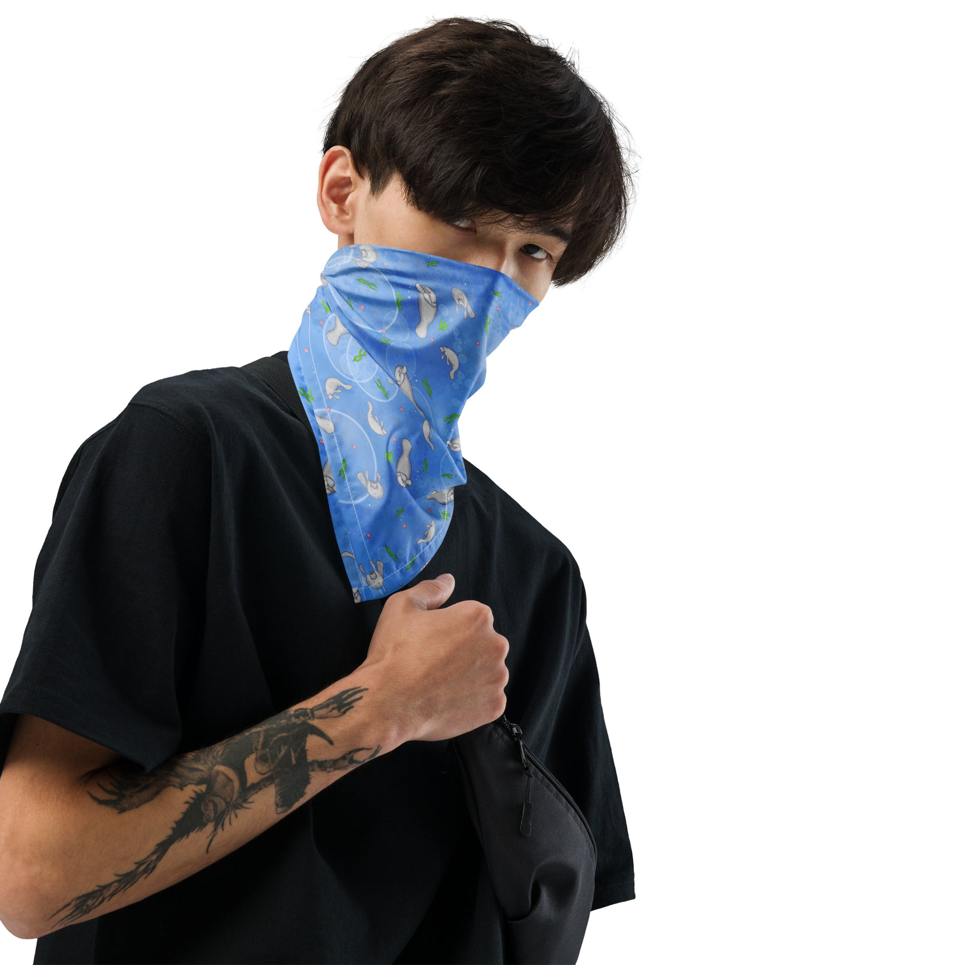 Manatee bandana. Shown as a bandana mask on a male model. Features patterned design of hand-illustrated manatees, seaweed, seashells, and bubbles on a blue  background.