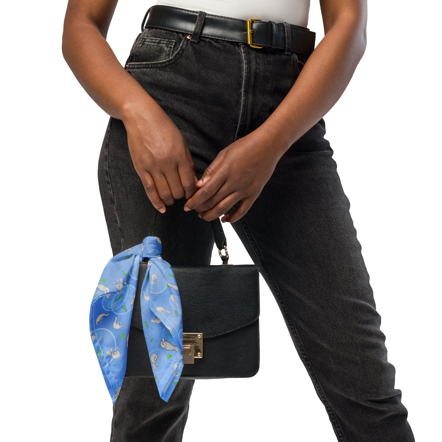 Manatee bandana. Shown as a ribbon accent on a purse. Features patterned design of hand-illustrated manatees, seaweed, seashells, and bubbles on a blue  background.