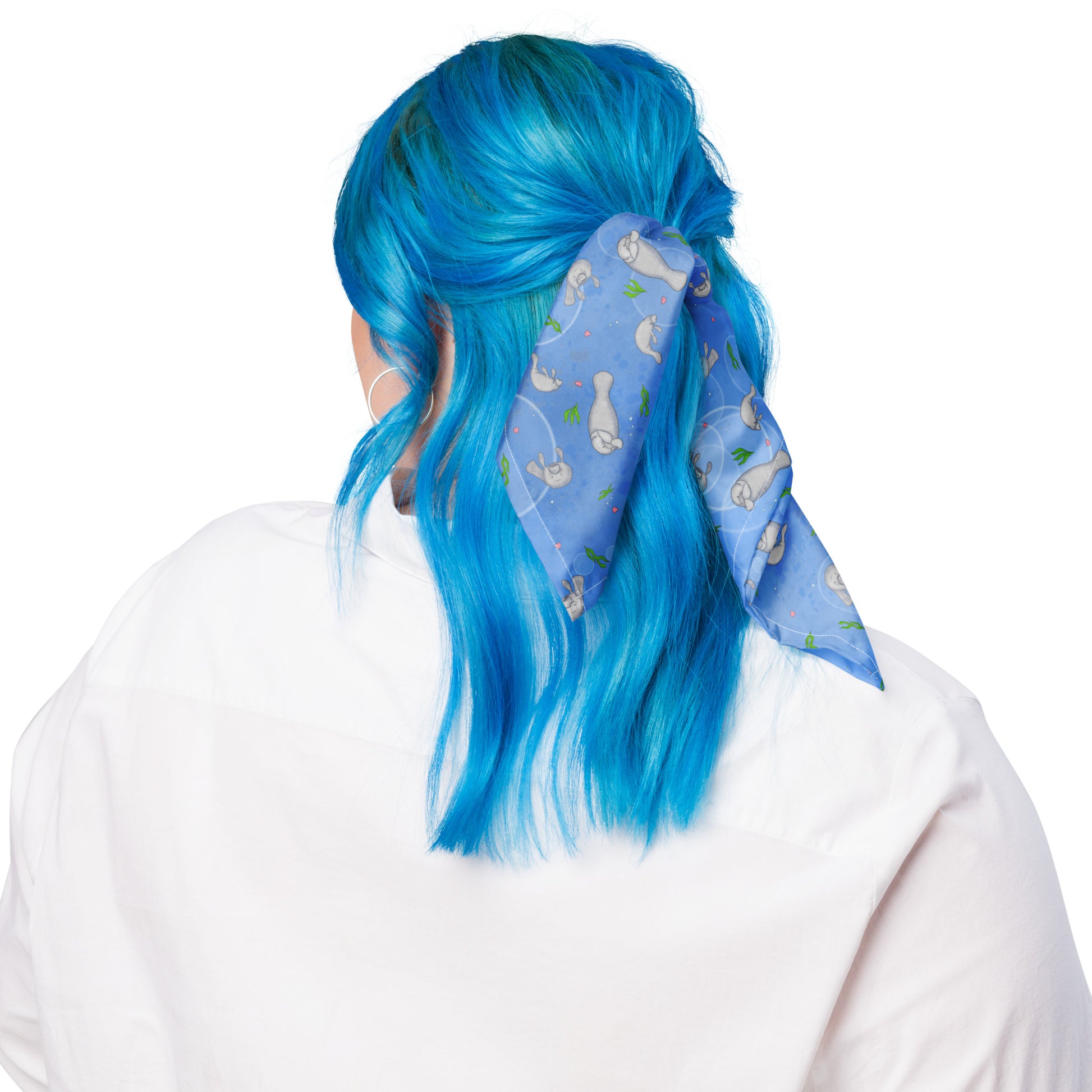 Manatee bandana. Shown as a hair ribbon on a female model. Features patterned design of hand-illustrated manatees, seaweed, seashells, and bubbles on a blue  background.