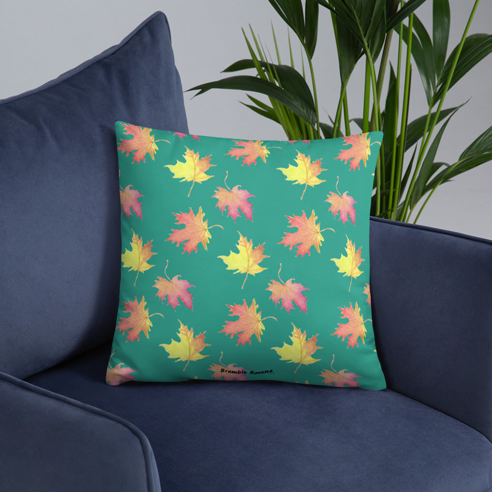 Front of 18 by 18 inch accent pillow featuring watercolor fall leaves on a dark green background. Pillow is double-sided. Larger patterned leaves on the back. Smaller patterned leaves on the front. Shown on a blue sofa.