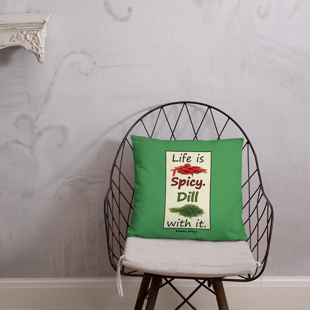 Life is spicy. Dill with it. Phrase with images of chili peppers and dill weed. Rectangular frame for saying on green background. 18 by 18 inch accent pillow. Double sided image. Shown on a wicker chair.
