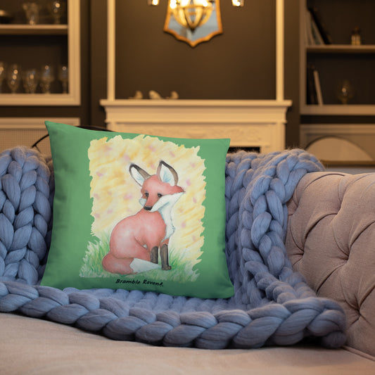18 by 18 inch accent pillow. Double-sided featuring original watercolor painting of a fox in the grass against a yellow backdrop. Pillow has a dark green fabric background. Shown on a blue knitted blanket ono a tan sofa.