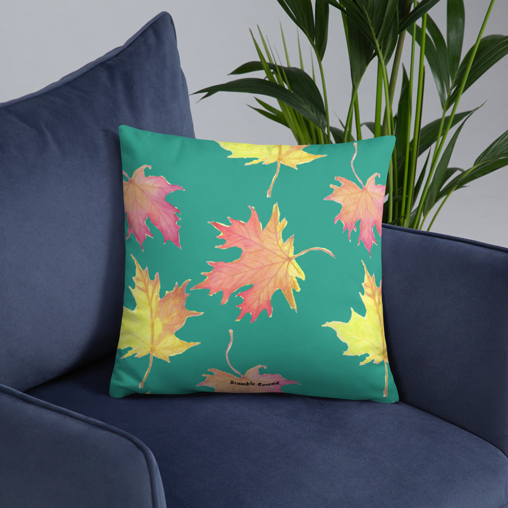 18 by 18 inch accent pillow featuring watercolor fall leaves on a dark green background. Pillow is double-sided. Larger patterned leaves on the back. Smaller patterned leaves on the front. Shown on a blue sofa.
