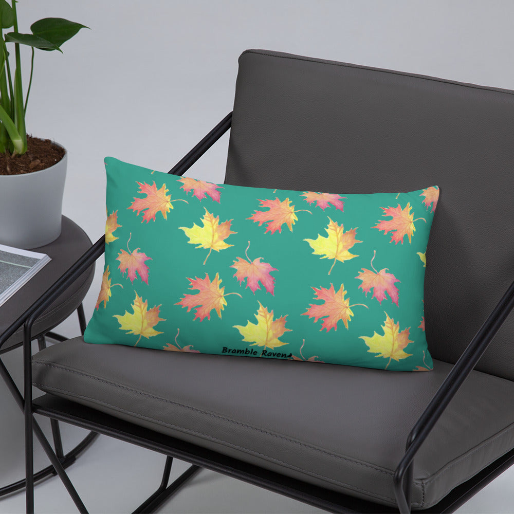 Front of 20 by 12 inch accent pillow featuring watercolor fall leaves on a dark green background. Pillow is double-sided. Larger patterned leaves on the back. Smaller patterned leaves on the front. Shown on a grey chair.