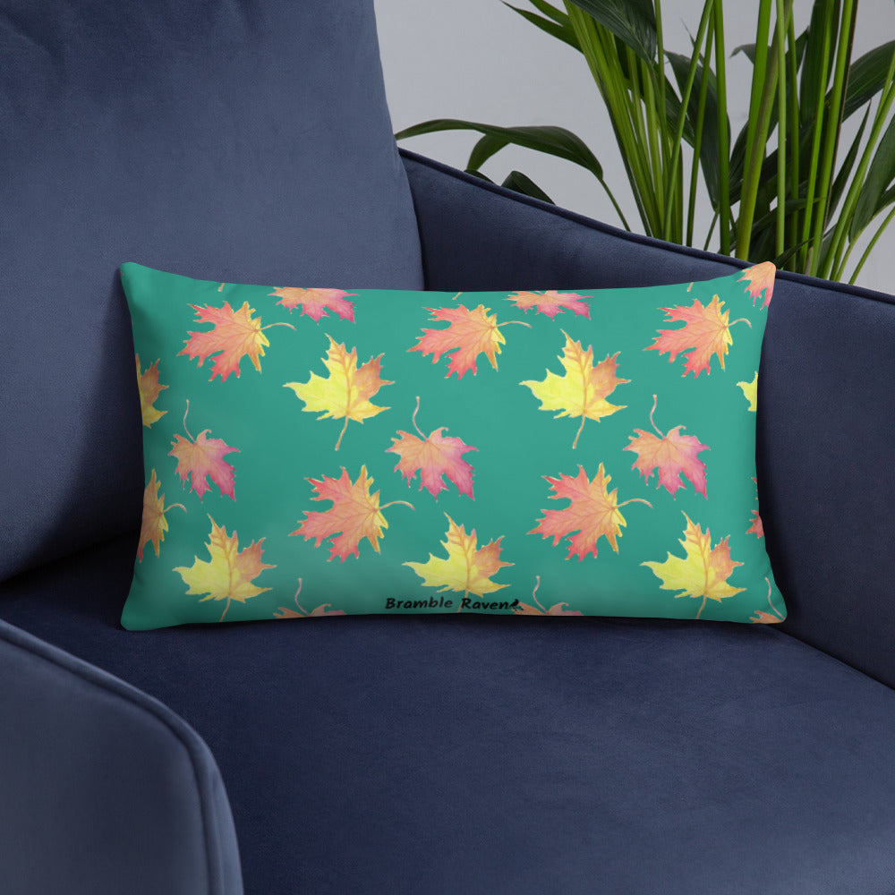 Front of 20 by 12 inch accent pillow featuring watercolor fall leaves on a dark green background. Pillow is double-sided. Larger patterned leaves on the back. Smaller patterned leaves on the front. Shown on a blue sofa.