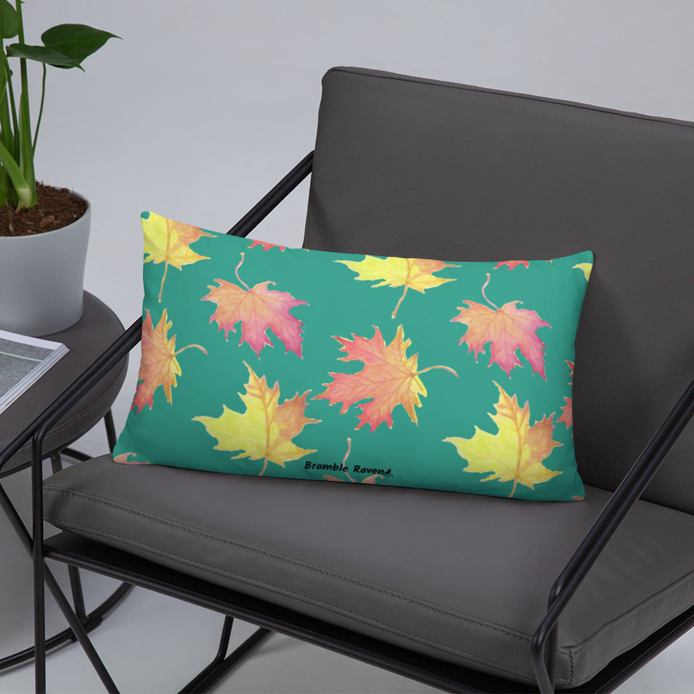 20 by 12 inch accent pillow featuring watercolor fall leaves on a dark green background. Pillow is double-sided. Larger patterned leaves on the back. Smaller patterned leaves on the front. Shown on a grey chair.