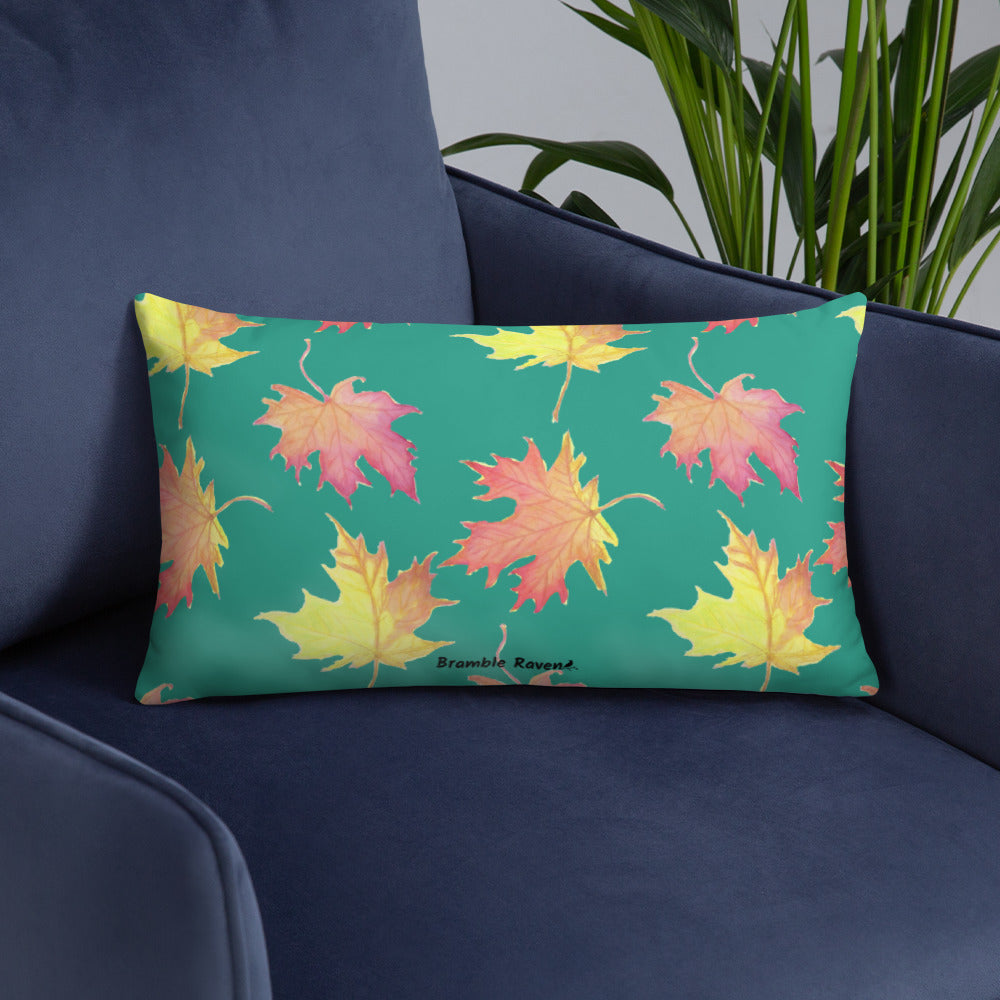 20 by 12 inch accent pillow featuring watercolor fall leaves on a dark green background. Pillow is double-sided. Larger patterned leaves on the back. Smaller patterned leaves on the front. Shown on a blue sofa.